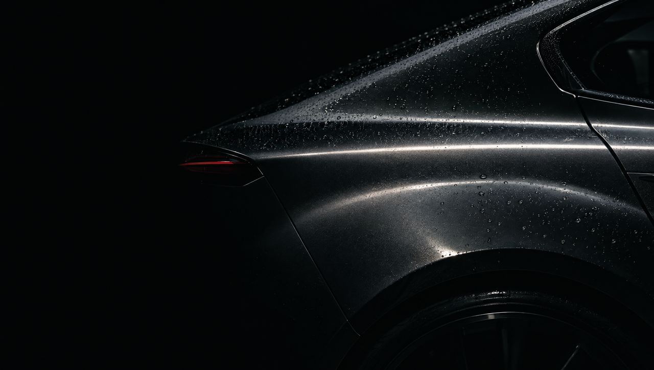 Detalle de la carrocería de un automóvil premium en un estudio oscuro, con una línea de luz sobre la pintura.